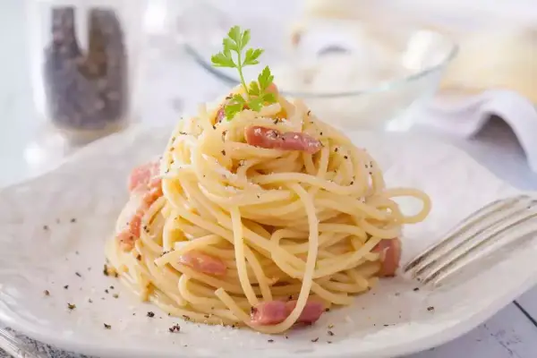 Un plat de tagliatelles carbonara crémeuses, garni de lardons et de persil frais, prêt à être dégusté.