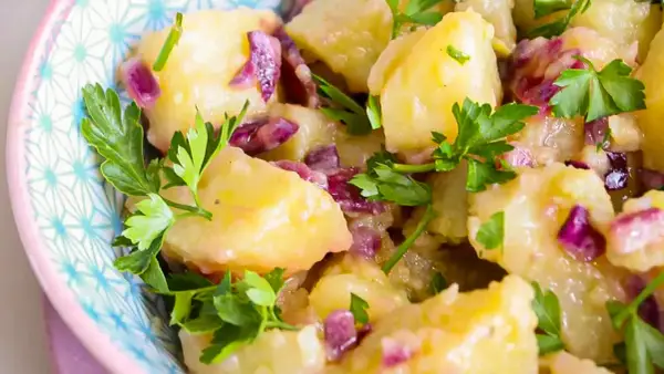 Salade de pomme de terre froide, garnie de persil frais et d'oignons rouges, servie dans un bol décoratif.