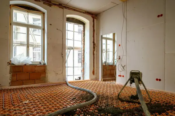 Installation d'un chauffage au sol ancienne génération, avec tuyaux orange et une machine de projection de chape.